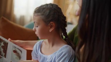 Akıllı çocuk evde ailesiyle birlikte kitap okuyor. Önemseyen anne, oturma odasındaki kanepede dinlenen komik kızıyla vakit geçiriyor. Kanepede mutlu bir anne ve çocuk bağı. Mutluluk