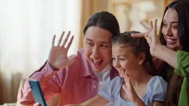 Neşeli akrabalar güneşli apartman dairesinde görüntülü görüşme yapıyorlar. Samimi evde cep telefonu kullanan, çocuklu, gülümseyen bir aile. Dijital cihazla konuşan çocuklu mutlu çift koltukta oturuyor.