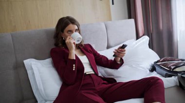 Rahat otel yatağında televizyon izleyen zarif bir iş kadını. Başarılı bir bayan kahve içip uzaktan kumandaya basıyor. Kırmızı elbiseli güzel bir kadın TV şovundan zevk alıyor.