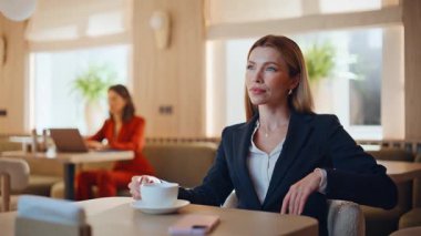 Açık kafe iç mekanında cappuccino yudumlayan şık bir bayan. Zarif takım elbiseli, modern kafeteryada kahve içen kendine güvenen bir kadın toplantı bekliyor. Başarılı bir iş kadını kafeteryada tatilin tadını çıkarıyor..