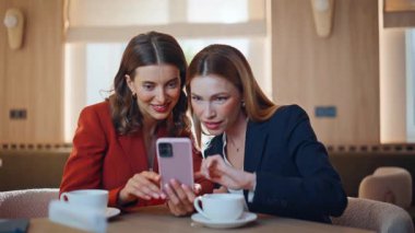 Kız arkadaşlar cep telefonlarını izleyip açık kafe içlerini kapatıyorlar. Restorandaki kahve molasında gülümseyen iş arkadaşları cep telefonlarının içeriğini kutluyorlar. İki iş kadını birlikte akıllı telefon kaydırıyor..