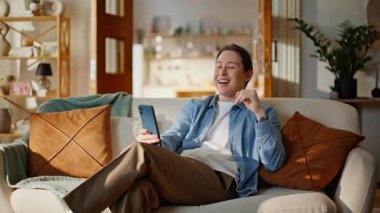 Kamerada gülümseyen adam akıllı telefondan konuşuyor. Kanepeye yakın oturuyor. Evde cep telefonuyla iş görüşmeleri yapan yakışıklı bir serbest yazar. Pozitif adam telefonda iş görüşmesi yapıyor.