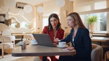 İş ortakları modern restorantta iş yerinde dizüstü bilgisayara bakıyorlar. İki zarif iş kadını bilgisayarda projeyi tartışıyor. Kafeteryada pazarlama stratejisinde işbirliği yapan gülümseyen kadınlar