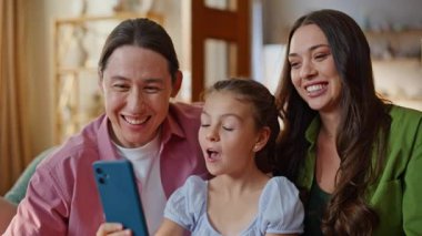 Neşeli bir aile, cep telefonunu kullanarak internet üzerinden konuşuyor. Mutlu baba, anne ve kız içeride modern cihazlarla görüntülü görüşme yapıyorlar. Hücre görüntüsü olan ebeveynler