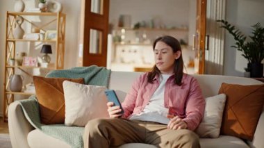 Evde akıllı telefon koltuğu kullanan rahat bir adam. Uzun saçlı Asyalı adam rahat koltukta cep telefonu sosyal ağları uygulamasına bakıyor. Pozitif yakışıklı esmer, cep telefonu görünümlü elektronik kitap okuyor.