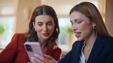 İş kadını, restorandaki kahve molasında arkadaşına cep telefonunu gösteriyor. İki zarif kadın öğle yemeğinde akıllı telefondan veri tartışıyorlar. Modern kafeteryada cep telefonu izleyen gülümseyen kadınlar.