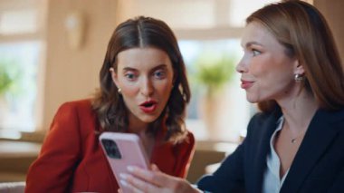 Şaşırmış arkadaşlar cep telefonlarına bakıyorlar. Kahvehanede iyi haberler alıyorlar. Yakın plan. Gülümseyen iki iş kadını cep telefonuna mesaj atıyor. İnternette tepkili duygusal kadınlar kafede birlikte kazanırlar..