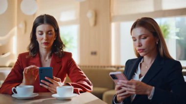 Restoran masasında kahve fincanlarıyla cep telefonlarına mesaj atan kendine güvenen kadınlar. Kafede cep telefonlarını karıştıran ciddi iş kadınları. Başarılı iş kadınları kafeteryada akıllı telefonlara mesaj atıyor.