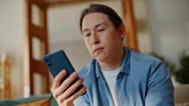 Kanepe oturma odasında akıllı telefon mesajı alan serbest çalışan hayal kırıklığına uğradı. Kaş çatan Asyalı adam cep telefonu ekranında duygusal tepki gösteren mesajlar okuyor. Kaybeden evde oturmakta zorlanıyor.