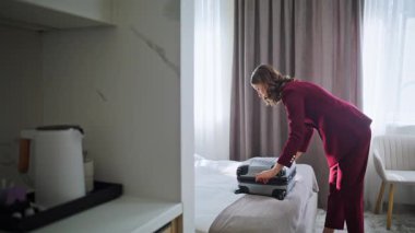 İş kadını rahat yatağa bavulunu boşaltıyor. Şık takım elbiseli iş kadını modern ışıklı otel odasında valizinden giysilerini çıkarıyor. Lüks bir motelde kendine güvenen bir kadın konuğu. Seyahat kavramı