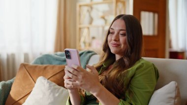 Rahat kız akıllı telefon mesajları okuyarak kanepeye yakın oturuyor. Gülümseyen genç bir kadın romantik bir ruh hali içinde erkek arkadaşından mesaj alıyor. Çekici, mutlu bir bayan, koltukta cep telefonunu kucaklıyor.