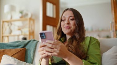 Akıllı telefon tutan düşünceli bir kız modern apartman dairesine mesaj yolluyor. Gülümseyen hayalperest kadın sosyal medyada geziniyor ve evde gülüyor. Neşeli bayan cep telefonu kullanarak erkek arkadaşıyla sohbet ediyor.