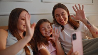 Hafif yatak odasındaki telefon görüşmeleri dinleniyor. Neşeli insanlar internette akrabalarıyla el sallayıp akıllı telefonlardan sohbet ediyorlar. Gülümseyen ebeveynler küçük kız birlikte cihaz kullanıyor.