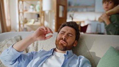 Baba baş ağrısı, kanepeye yaslanma, migren ağrısı. Gürültücü çocuklar babalarının dikkatini dağıtıp oturma odasındaki kanepede oyuncaklarla oynuyorlar. Yorgun baba kaosa tepki veriyor. Ebeveynlik stresli anlar