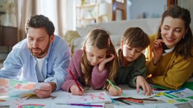 Veliler kâğıt üzerinde kalem çiziyor. Dairenin zeminini kapatıyorlar. Gülümseyen baba, çocuk yaşta anne, evde eğlenen çizimler yapıyor. Aile hafta sonu birlikte. Çocukluk eğlence aktivitesi