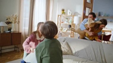 Dört akraba evde oturup sohbet ediyorlar. Neşeli çocuklar, kaygısız ebeveynler oyuncaklar fırlatıp kanepeye sıçrayıp birlikte gülüyorlar. Gülümseyen anne baba küçük çocuklar aktif oyundan zevk alıyor.