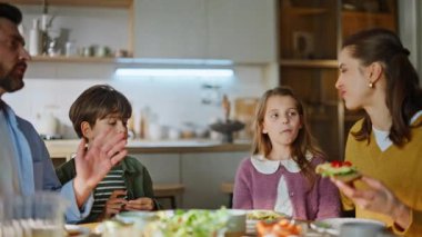 Konuşan akrabalar kahvaltıyı paylaşıyor. Parlak, modern mutfağa yakın oturuyorlar. Yakışıklı baba portakal suyu dolduruyor, karı-koca iletişimi kuruyor. Rahatlamış aile sağlıklı sabah rutininin tadını çıkarıyor.