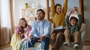 Anne oğul, hayal kırıklığına uğramış baba kız oturma odasıyla oyun oynayarak online kazanmayı kutluyor. Heyecanlı rekabetçi çocuk gülüyor zafer şaka kaybediyor kız kardeş yumuşak yastık kanepesinde birlikte oturan