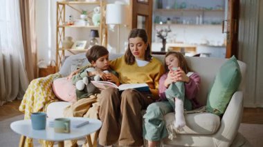 Anne çocuklar kitap oturmaktan zevk alıyorlar. Aile hafta sonunun tadını çıkarıyorlar. Mutlu gülümseyen anne, sevimli çocuklara evde sakin vakit geçirmeleri için masal okuyor. Neşeli kadın, ergen kız, oğul bağı kuruyor.