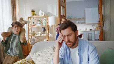 Migreni olan baba evde kanepeye kapanarak acı çekiyor. Gürültücü çocuklar babalarının dikkatini dağıtıyor oyuncaklar oynayıp apartman dairesi diye bağırıyorlar. Şakakları ovalayan yorgun sakallı adam evde baş ağrısı hissediyor.