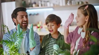 Neşeli akrabalar mutfaktaki çiçekleri sularken el çırpıyorlar. Bakıcı anne akıllı telefon kayıt işlemini tutuyor. Sevimli çocuklar babalarına beşlik çakarken saksı bitkilerinin keyfini çıkarırken yardım ediyorlar.