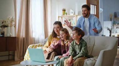 Anne çocuklar oturma odasındaki koltuğu selamlıyorlar. Neşeli baba sohbete katılıyor. Pozitif aile, akrabalarıyla oturma odasında dizüstü bilgisayarla internet bağlantısı kuruyor. Modern teknoloji