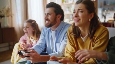 Ebeveynler, çocukların elleri konsol oturma odasında yakın plan oynuyorlar. Baba kız, hayal kırıklığına uğramış anne oğluyla çevrimiçi video oyunu kazanıyor. Heyecanlı genç kız zaferi kutluyor kendiyle gurur duyuyor.