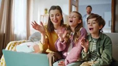 Yakından güzel bir aile dizüstü bilgisayarı arıyor ve düz ışıkta el sallıyor. Mutlu ebeveynler kameraya gülümseyip akrabalarıyla görüntülü konuşma yapıyorlar. Çevrimiçi konuşan neşeli insanlar modern teknolojinin tadını çıkarıyor