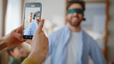 Eller gözleri bağlı bir şekilde video çekiyor. Maçın tadını çıkarıyor. Ebeveynler hafta sonları evde oynuyorlar. Gözleri bağlı çocuklar eğleniyor. Kadın anne video kaydediyor. Mutlu aile hafta sonu aktivite konsepti