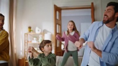 Neşeli aile dans ederken rahat bir ışık dairesi yakın plan. Mutlu ebeveynler, küçük çocuklar eğlenceli hareketler yapıyor ve evde eğleniyorlar. Gülümseyen genç anne baba, hafta sonunu birlikte geçirerek şaka yapıyor.