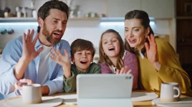Aile ve çocuklar tableti videoya alıyor. Mutfağı kapatıyorlar. Gülümseyen anne baba küçük çocuklar sanal toplantı yapıyor webcam gibi görünüyor uzaktan sohbetin keyfini çıkarıyorlar.