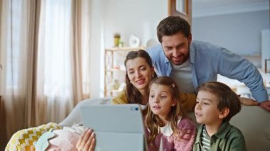 Mutlu akrabalar online toplantıda web kamerası tabletine bakıyorlar. Gülümseyen sakallı baba videosu genç çocuklar ve eşiyle rahat koltukta birlikte arıyor. Modern aile teknolojisi