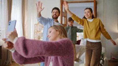 Liseli kız, aile evi ile yakın çekim videosu çekiyor. Ergen, elinde akıllı telefon tutarak aile kardeşiyle fotoğraf çekiyor. Mutlu insanlar el sallayarak cep telefonu kameralarını içeri çekiyor.