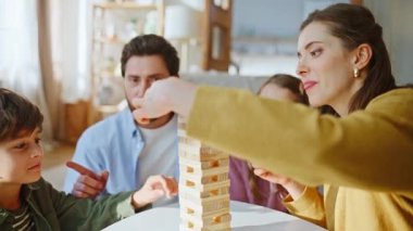 Neşeli bir aile, Jenga oynayarak evde oturma odasının keyfini çıkarıyor. Küçük çocuk tahta bloğu kulenin tepesindeki dengeye yerleştiriyor. Anne, baba, kız kardeş, çocuğu evde destekliyor.