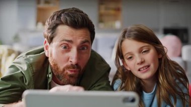 Baba kız oturma odasının zemininde video tableti izliyor. Mutlu sakallı baba gülümseyen reşit olmayan kız çocuk aile saatinde online içeriğin tadını çıkarıyor. Kaygısız çocuk birlikte konuşuyor..