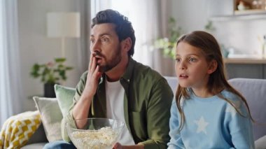 Ebeveyn kızı gerilim filmi seyrediyor. Rahat rahat kanepeyi kapatıyorlar. Korkak sakallı baba elinde patlamış mısır kasesi, gözlerini kapatıyor ve televizyon izlemekten keyif alıyor. Baba, genç kız filmde oynuyor..
