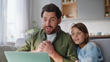 Baba çocuk modern oturma odasındaki dizüstü bilgisayarlı web kamerasının keyfini çıkar. Gülümseyen sakallı adam mutlu çocukluk videosu rahat koltuğu arıyor. Baba-kız muhabbeti.