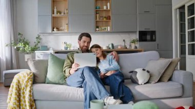 Baba kızı rahat bir kanepede otururken tableti karıştırıyor. Mutlu kaygısız baba ergen kız online video izleyip rahat rahat oturma odası kanepesinde dinleniyor. Sıradan aile eğlencesi konsepti.