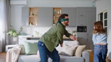 Gözleri bağlı bir baba, kızı evde oyun oynarken yakalıyor. Saklambaç oynayan küçük bir çocuk. Mutlu baba, neşeli kız, gülen koltuk, kucaklaşan mutluluk..