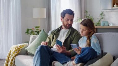 Babam akıllı telefon kızına rahat bir kanepede oturduğunu gösteriyor. Gülümseyen sakallı baba, internetteki içeriği tartışan çocukluk çağındaki kızı rahatlattı. Modern cep telefonu etkileşimi.