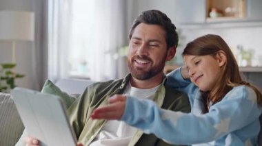 Baba kız tablet örtülü kanepede fotoğraf aşırıyor. Yakın çekim. Gülümseyen baba kızı internetten bilgisayar ekranı almayı seçiyor. Mutlu aile oturup dijital aygıt izliyor..