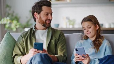 Mutlu ebeveyn çocuk cep telefonları rahat koltuklarda oturuyor. Kaygısız baba kızı cep telefonlarını karıştırırken sakin bir ailede dijital dünyaya dahil oldu. Akıllı telefon bağımlılığı.