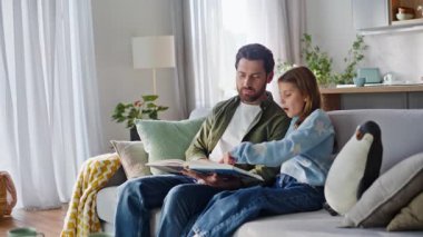 Baba kız kitap dinlemekten zevk alıyor. Gülümseyen baba rahat koltukta oturan edebiyat okuyan tatlı kız çocuğu. Mutlu ebeveyn çocuk çevirme sayfaları aile eğitimi hobisi içeriyor.