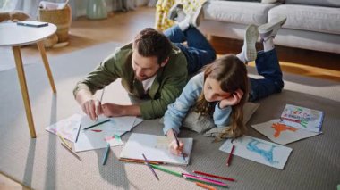 Baba çocuk yerde yatmayı da içeriyor. Mutlu baba, yetenekli kız renkli kalemler yapıyor güneşli oturma odasında yaratıcı hobilerin tadını çıkarıyor. Baba çocuk birlikte resim çiziyor..