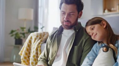 Baba çocuk tablet daire zeminini tarıyor. Sevimli prematüre kız babasının omzuna yaslanıyor bilgisayarını izliyor ve hafta sonu birlikte oturup rahatlıyor. Mutlu adam kızına içeriğini gösteriyor..