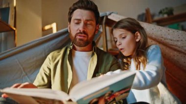 Çocuk battaniye kalesi okuyordu. Gülümseyen bir baba, mutlu bir kızın el yapımı sığınma evini paylaşıyor. Neşeli aile sayfalarını çevirerek hikaye anlatmayı sever. Bekar baba