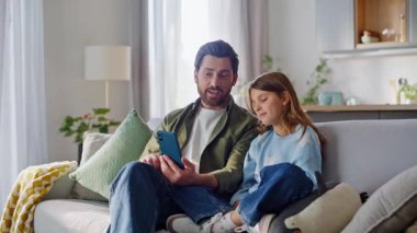 Baba kızı, hafta sonu evde rahat rahat oturup cep telefonu haberlerini tartışıyor. Gülümseyen sakallı baba sevimli çocukla konuşuyor. Akıllı telefon ekranı birlikte sosyal medyada geziniyor..