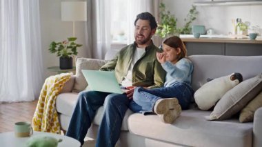 Erkek kız, internet üzerinden akrabalarını karşılamak için web kamerası tableti sallıyor. Gülümseyen sakallı baba, reşit olmayan kız videosu rahat bir kanepe için arıyor. Modern aile teknolojisi bağlantısı.