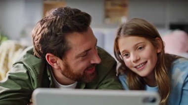 Gülen baba kız çizgi film seyrediyor tablet evde uzanıyor birlikte çay içiyor yakın plan çekiyoruz. Mutlu baba kızı, online eğlence videosu bilgisayarının aile hafta sonu dairesinde eğleniyor..