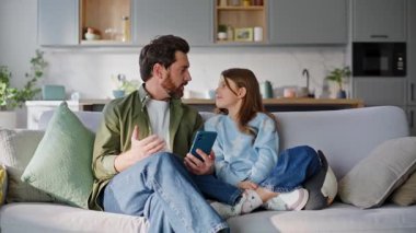 Akıllı telefon web kamerası sallayan baba çocuğu rahat bir kanepede oturuyor. Olumlu baba kızı internette konuşuyor. Haberleri tartışıyor. Dairede cep telefonu internet uygulaması kullanıyor. Aile video çağrısı.